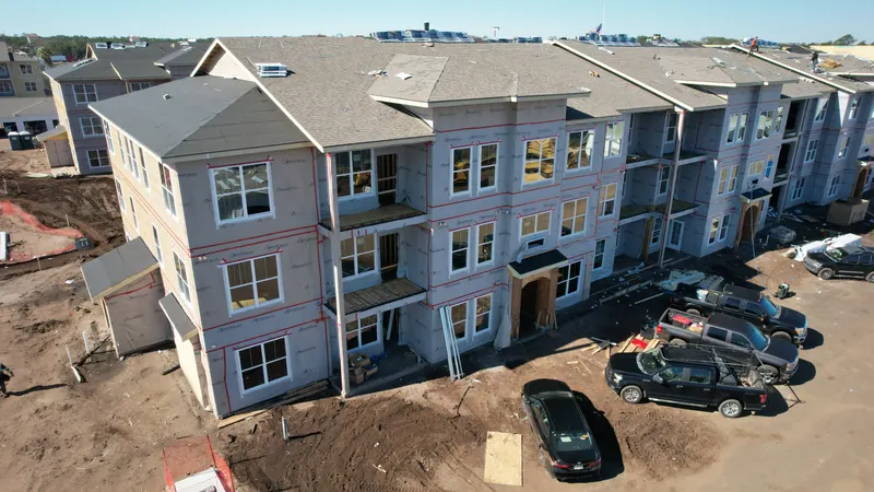 Aerial view of a three-story building with a finished shingled roof, wrapped walls, and framed balconies.