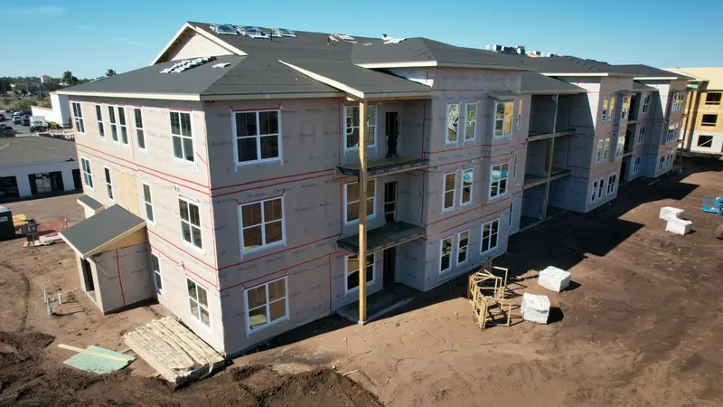 Aerial corner view of a three-story building with the roof complete and the walls wrapped, balcony openings framed on the near face.