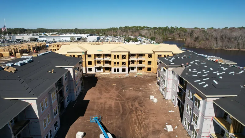 Aerial view of the courtyard between two dried-in buildings and a third with fresh roof sheathing, a lift working in the open yard between them.