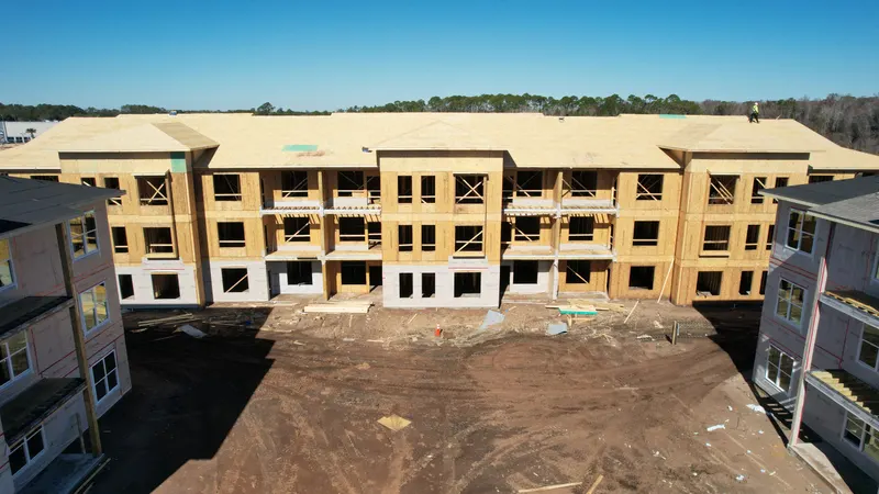 Aerial view of a long building with fresh roof sheathing laid over the set Howland trusses and open three-story framing below.