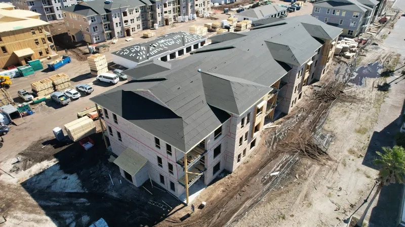 Aerial view of a nearly complete three-story building with a dark shingled roof and wrapped walls.