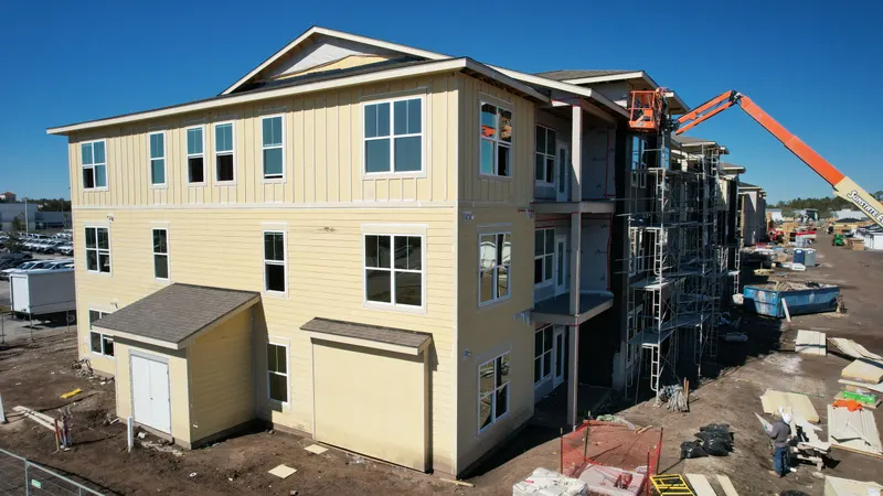 Low aerial of a yellow-sided three-story building with a telehandler working the far end of the elevation.