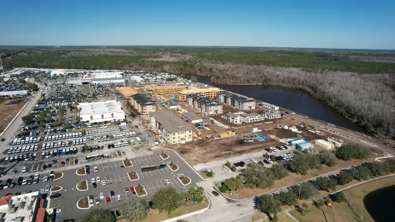High aerial of the full development beside a river, with the surrounding retail center and parking in the foreground.