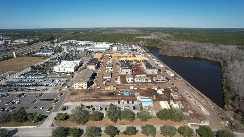 High aerial of the residential development with a large pond on one side and a commercial corridor on the other.
