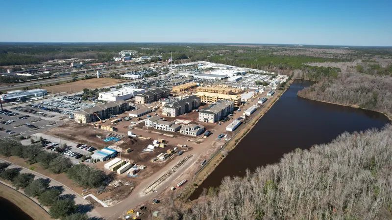 High aerial looking across the development, with buildings at several stages of construction and water along the far edge.