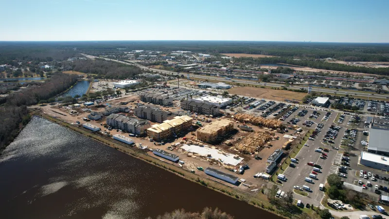 High aerial taken from over the water, showing the development across the river with parking lots beyond it.