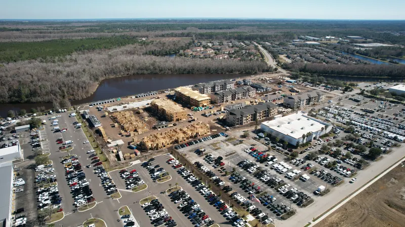 High aerial of the development with a large parking area in the foreground and the river along the far side.