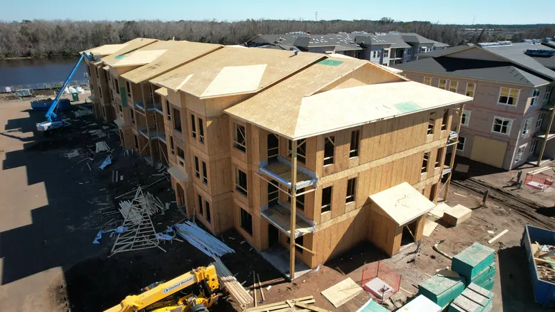 Aerial view of a building with fresh roof sheathing laid over the set Howland trusses, a boom lift and a telehandler working alongside it.